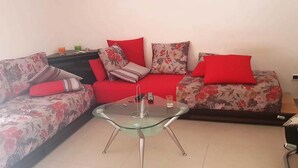 Ein Wohnzimmer mit einem Glastisch, zwei Sofas mit floralem Bezug und roten Kissen.