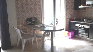Een compacte keuken met een eethoek, met een ronde tafel, twee stoelen, een raam met zonwering en een ingebouwde oven.
