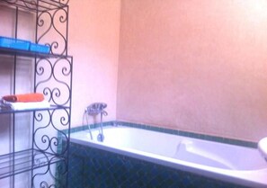 Ein Badezimmer mit einer Badewanne, einem Regal mit einem Handtuch und einem Metallregal.