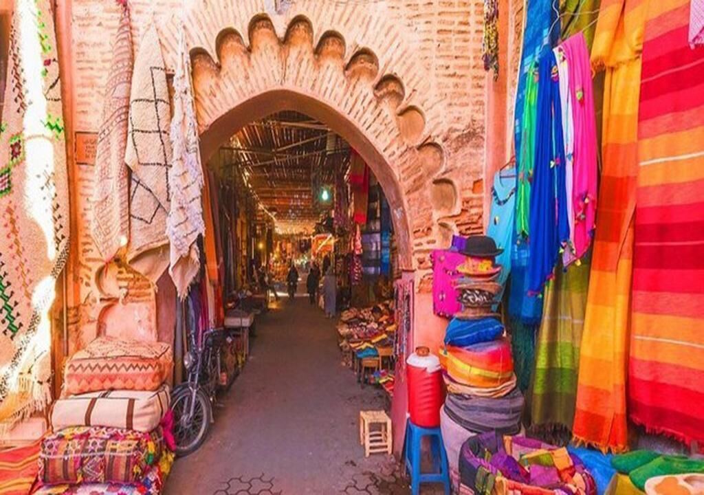 A narrow market street with colorful textiles and rugs displayed on both sides.
