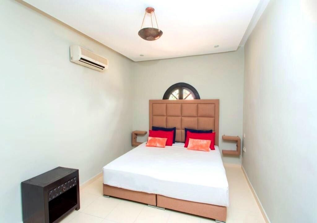 A bedroom with a bed, a nightstand, an air conditioning unit, and a ceiling light fixture.