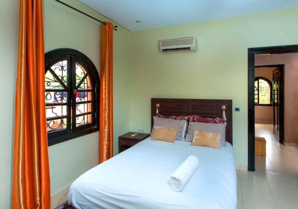 Un dormitorio con cama, cortinas, aire acondicionado y una ventana con celosía decorativa.