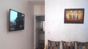 A living room with a flat-screen TV mounted on the wall, a sofa with patterned cushions, and a framed painting above the sofa. - Apartment 5 minutes from the beach 4253 (Saidia)
