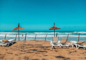 A beach with white lounge chairs and thatched umbrellas. - Apartment 5 minutes from the beach 4253 (Saidia)