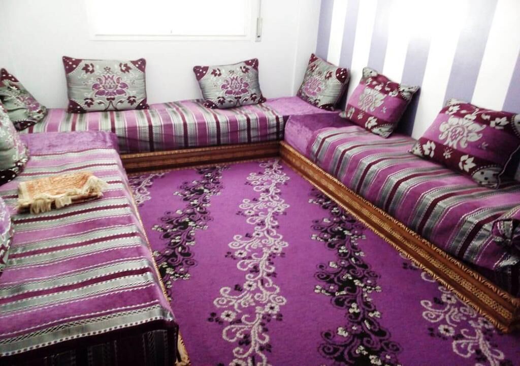 Une pièce avec une moquette violette, une literie à rayures et des coussins à motifs.