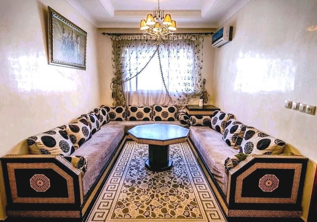A room with a sofa set, a central table, patterned floor, and a chandelier.