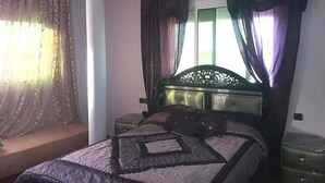 A bedroom with a bed, a nightstand, a lamp, and a window with curtains. - Sea View Apartment in the center of Oued Laou 4208 (Oued Laou)