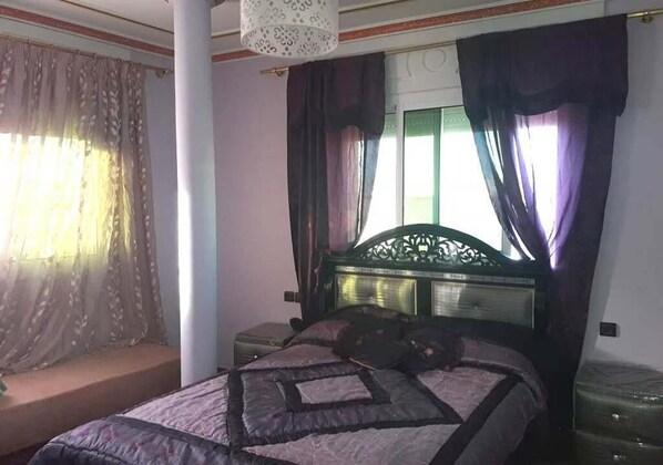 A bedroom with a bed, a nightstand, a lamp, and a window with curtains.