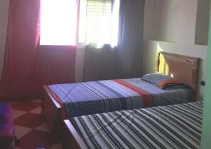 Ein Zimmer mit zwei Einzelbetten, einem Fenster mit Vorhängen und einem Schachbrettfußboden.