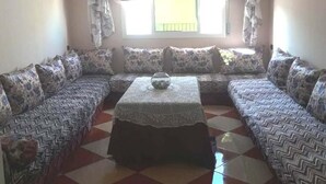 A living room with a sofa set, a coffee table, and a window with curtains. - Sea View Apartment in the center of Oued Laou 4208 (Oued Laou)