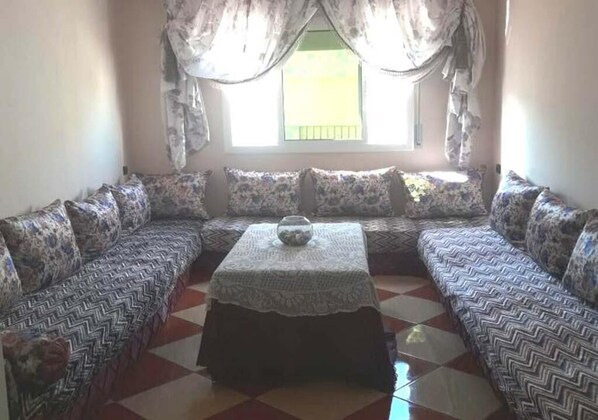 Ein Wohnzimmer mit einer Sofagarnitur, einem Couchtisch und einem Fenster mit Vorhängen.