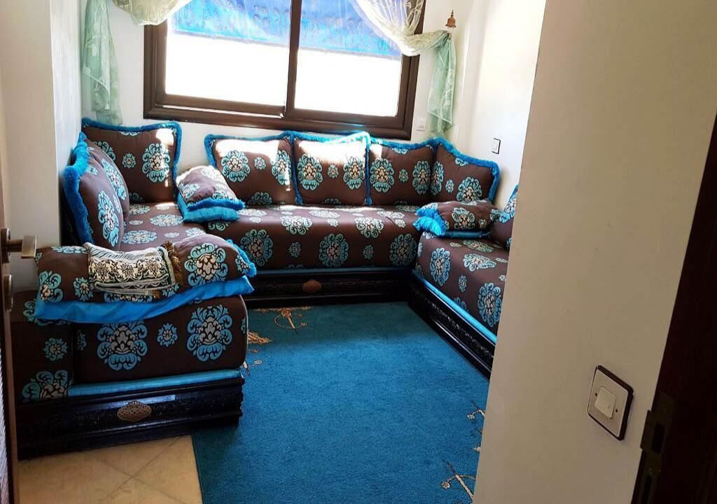 Ein Ecksofa mit gemustertem Stoff, ein blauer Teppich und ein Fenster mit Vorhängen.