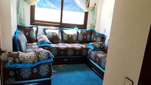 Un sofá de esquina con tela estampada, una alfombra azul y una ventana con cortinas.