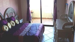 Un dormitorio con una cama, dos sillas de mimbre, una mesita y un espejo.