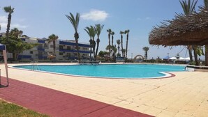 Une piscine bordée de rouge, entourée de palmiers et d’un bâtiment dont les murs extérieurs sont peints en bleu et en blanc.