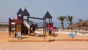 Une aire de jeux avec un toboggan, des structures d’escalade et un petit abri.