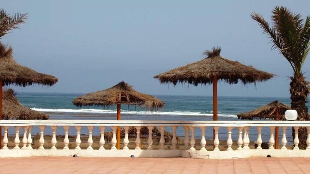 Une vue sur la plage, avec des parasols en chaume et une balustrade blanche.