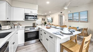 Une cuisine moderne avec des meubles blancs, un îlot central et un coin repas doté de chaises en bois.