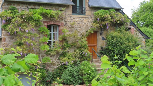 A stone house with a steeply pitched roof, a wooden door, and a window with a metal balcony.