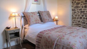 Une chambre à coucher avec un lit, deux lampes de chevet, une table de chevet, une petite table et un mur en pierre.