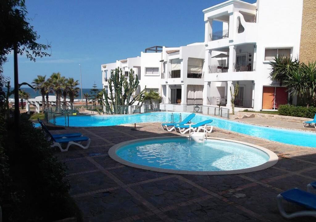 A pool area with blue lounge chairs, a circular pool, and a white building with balconies.
