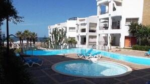 A pool area with blue lounge chairs, a circular pool, and a white building with balconies.