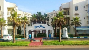 A hotel named 'Beach House' with a central entrance, palm trees, and a parking area.