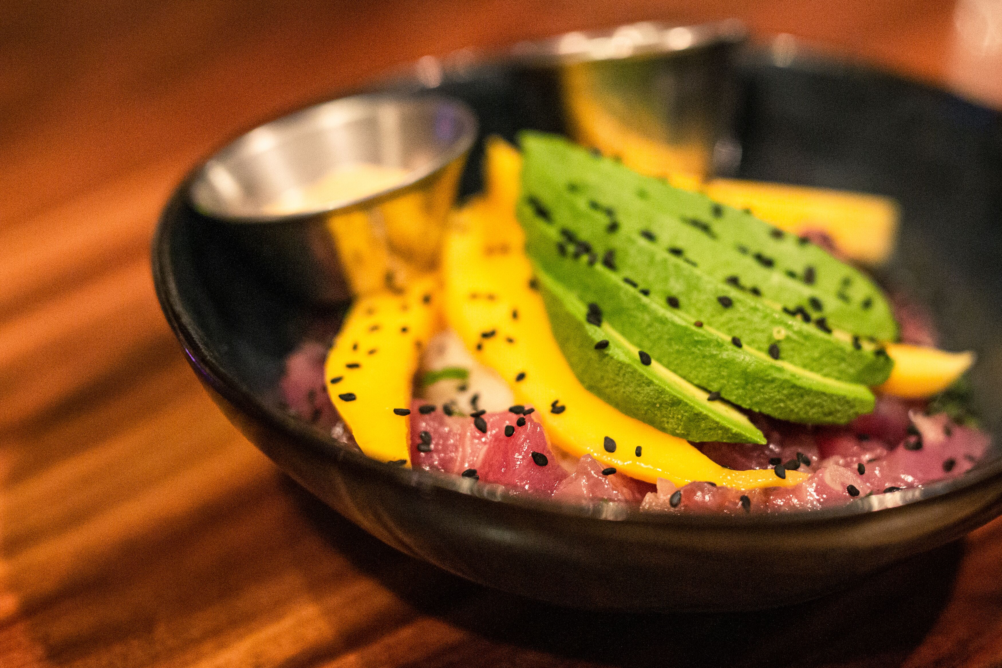 Un tazón de pescado crudo cubierto de aguacate, mango y semillas de sésamo negro.