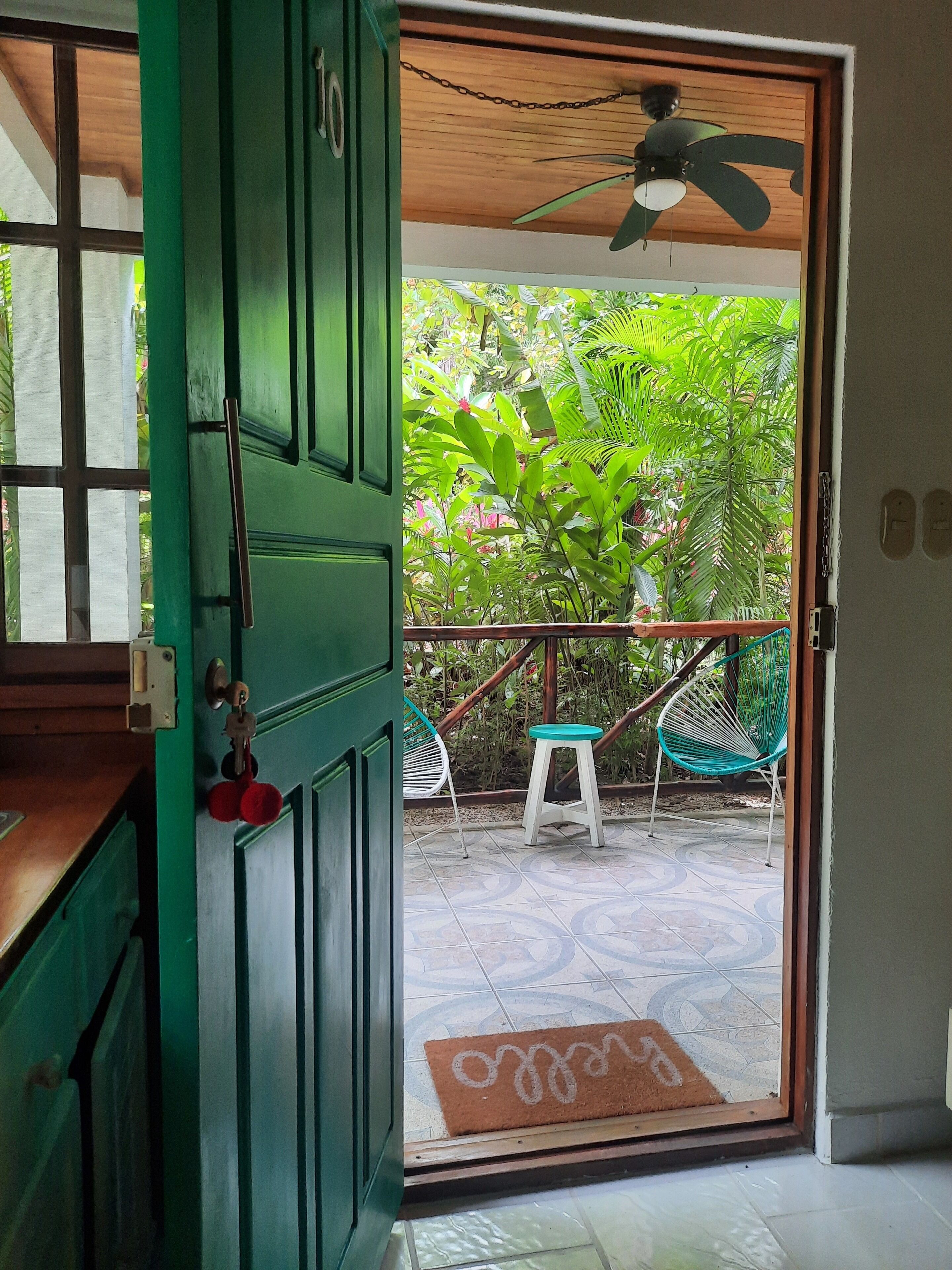 A green door leading to a covered outdoor area with a ceiling fan, a small white stool, and a green hammock chair.