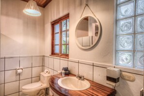 Et badeværelse med et træbord, et rundt spejl, et toilet og et vindue med dekorativt glas.