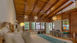 A wooden cabin bedroom with a large bed, two hanging light fixtures, and a desk area.