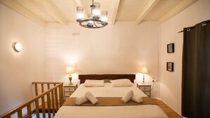 Een net opgemaakt bed met witte lakens en handdoeken, een houten hoofdbord en twee bedlampjes.