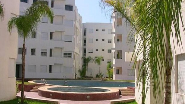A courtyard with a swimming pool, surrounded by multi-story buildings with balconies. - Apartment in Bouznika 4287 (Bouznika)