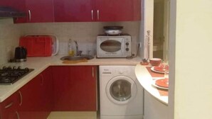 A compact kitchen with red cabinets, a microwave, a washing machine, and a gas stove. - Apartment in Bouznika 4287 (Bouznika)
