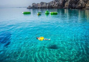 A clear blue sea with a person floating on a yellow board, surrounded by green floating rings.