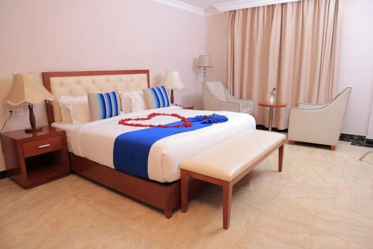 A hotel room with a bed, bedside tables, a bench, a chair, and a small table.