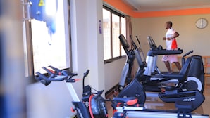 A gym with stationary bikes and treadmills, a clock on the wall, and a window with curtains. - Tolip Olympia Hotel (Addis Ababa)