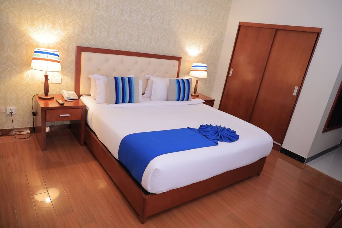 A neatly made bed with a blue accent, two bedside lamps, a wooden nightstand, and a wooden wardrobe.