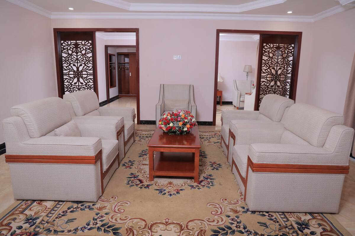 A hotel lobby with two sofas facing each other, a wooden coffee table with a floral arrangement, and a patterned carpet.