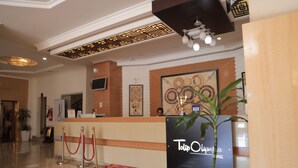 A hotel reception area with a reception desk, a red carpet, a potted plant, and a wall with a framed artwork. - Tolip Olympia Hotel (Addis Ababa)