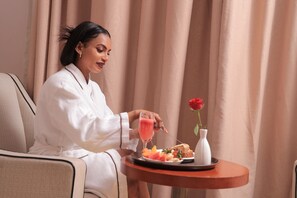 A person sitting on a chair with a tray containing food and a drink, a rose in a vase, and curtains in the background. - Tolip Olympia Hotel (Addis Ababa)