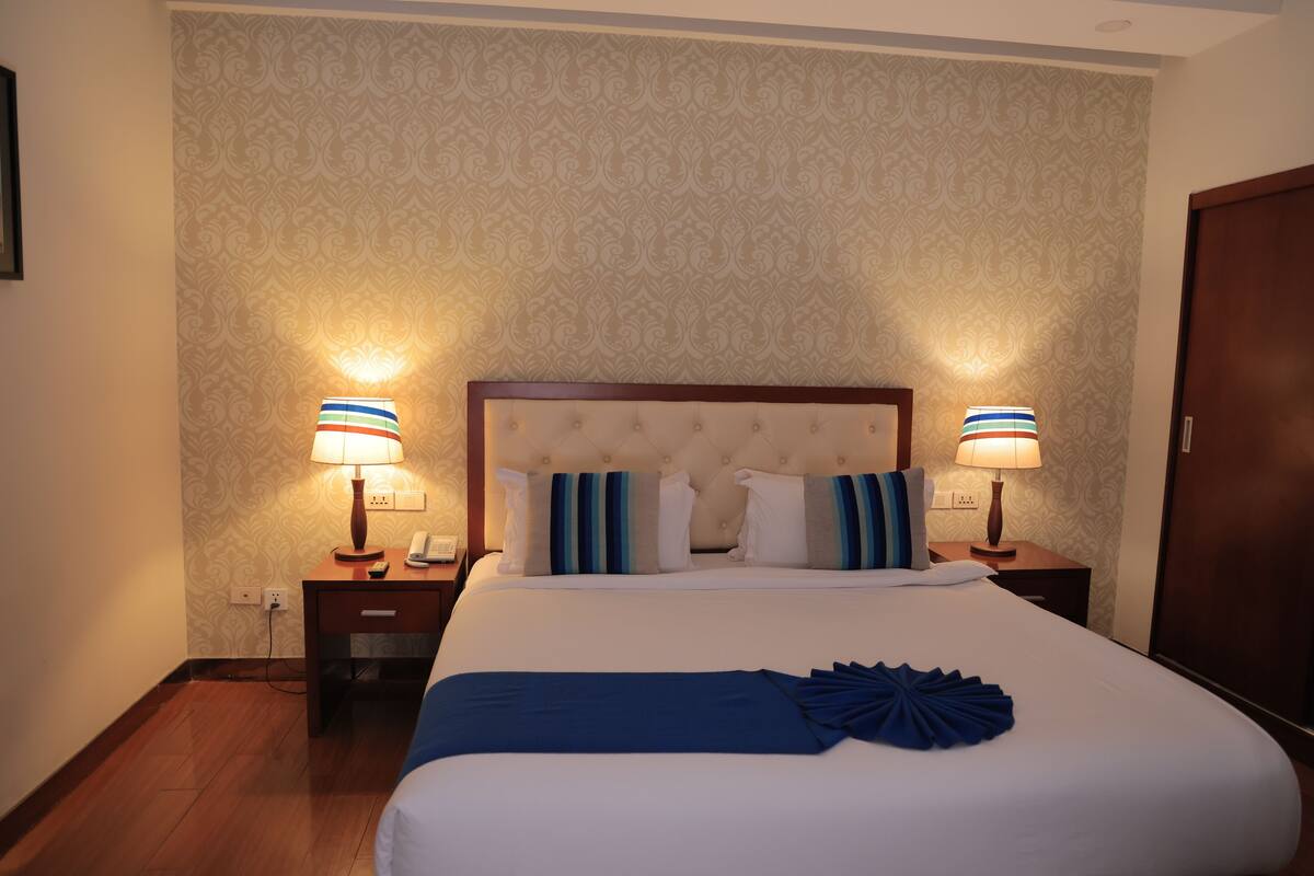 A hotel room with a large bed, two bedside lamps, a wooden headboard, and patterned wallpaper.