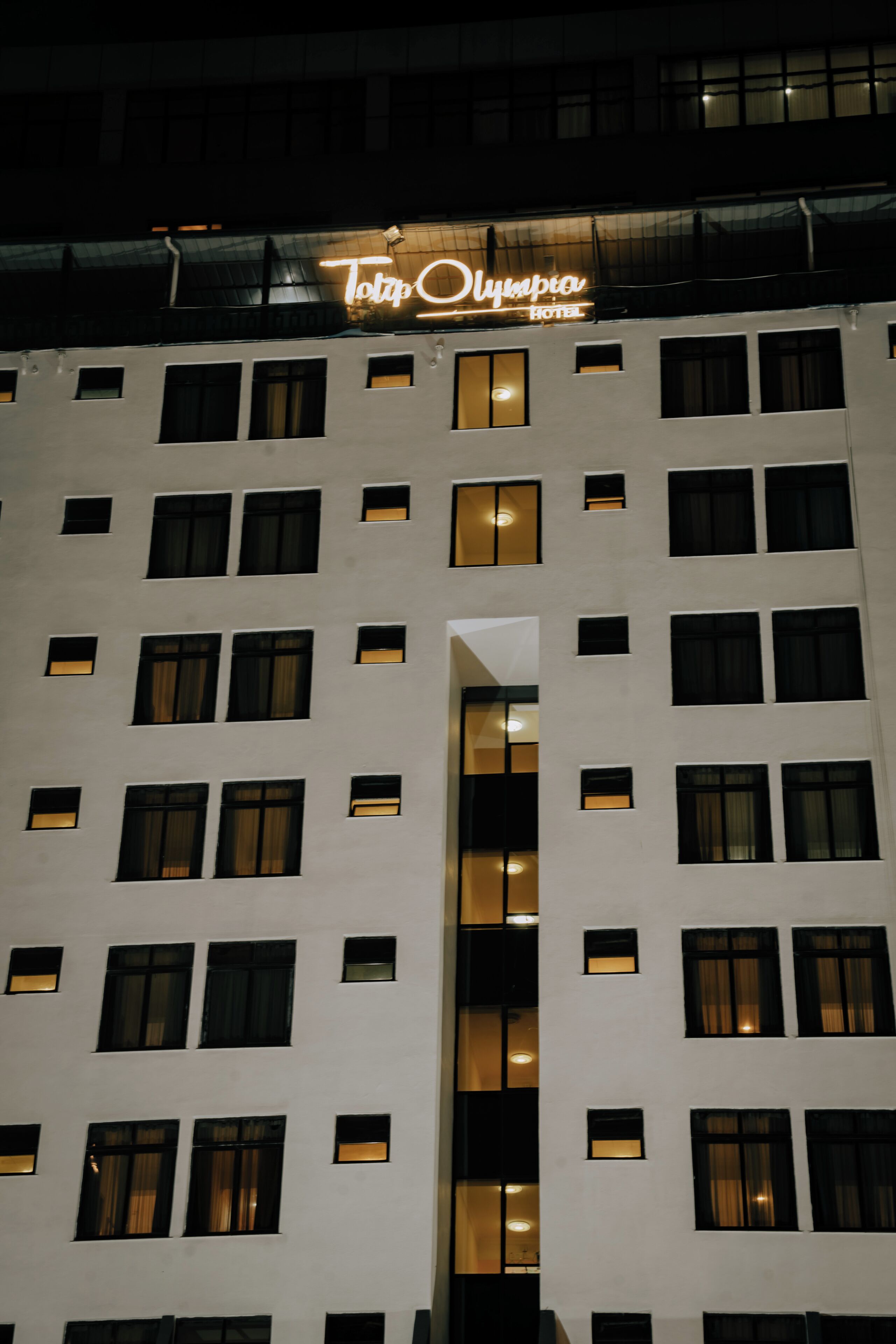 A hotel building with multiple windows and a neon sign above the entrance.