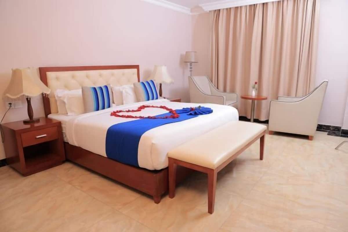 A hotel room with a bed, bedside tables, a bench, a chair, and a small table.