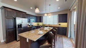 A modern kitchen with dark cabinetry, stainless steel appliances, a granite countertop, and a dining area with chairs. - PVZ40|Steps to Pools *SplashPad* HotTub*GreenSpace (Santa Clara)
