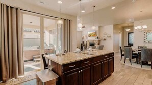 A modern kitchen with a large island, dark cabinetry, and pendant lighting. - PVZ40|Steps to Pools *SplashPad* HotTub*GreenSpace (Santa Clara)