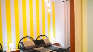 Ein Schlafzimmer mit einem Bett, zwei Nachttischen, einer Lampe und einer Wand mit vertikalen gelb-weißen Streifen.