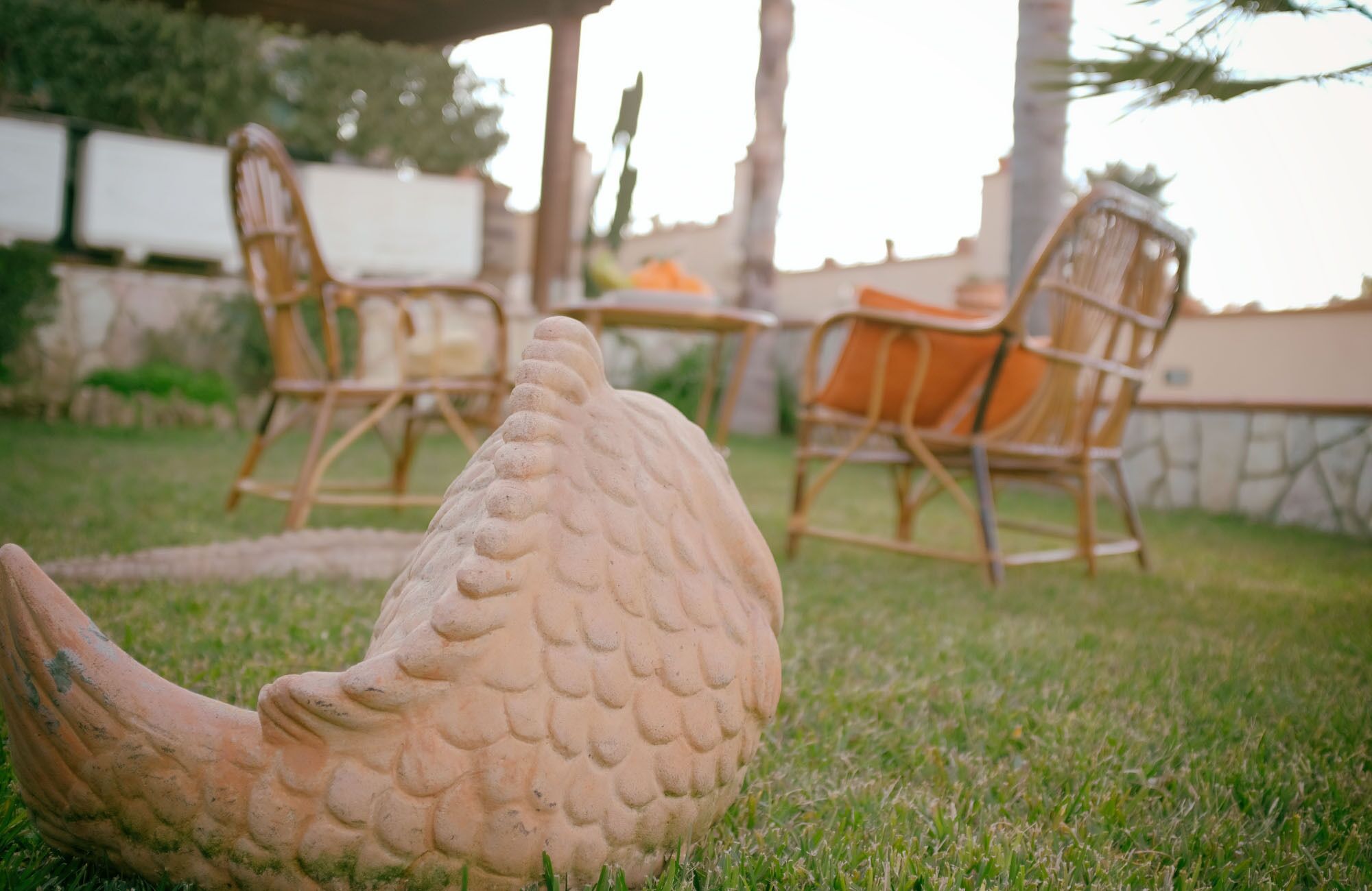 A garden with a stone fish sculpture, wicker chairs, and a table.