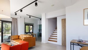 A modern living room with a sofa, a red chair, a dining table, and a staircase leading to an upper floor. - Private swimming pool, amazing views, sleeps 6. (Rethymno)