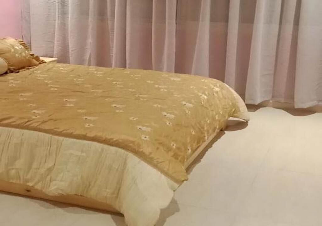 A bed with a patterned bedspread, a pillow, and a curtain in the background.